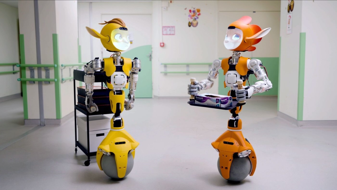 Les robots Miroki et Miroka dans un couloir d'hôpital, l'un portant un plateau